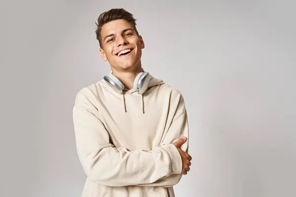 Handsome young guy in headphones smiling with folded arms against light background — Stock Photo