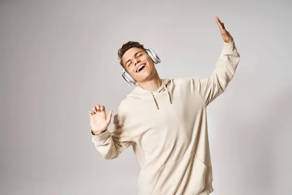 Charming student in white hoodie dancing to music with closed eyes on light background — Stock Photo