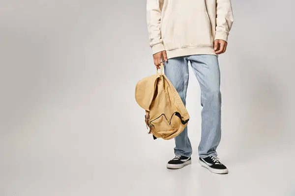 Обрезанный снимок студента в повседневной одежде, стоящего с рюкзаком на сером фоне — стоковое фото