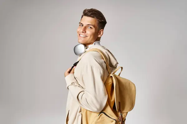 Smiling student in headphones and casual outfit with backpack looking from behind back — Stock Photo