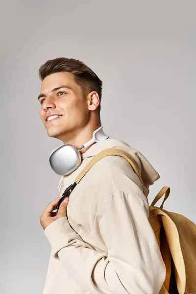 Веселий студент в навушниках і повсякденному вбранні з рюкзаком стоячи в бік і дивлячись вгору — стокове фото