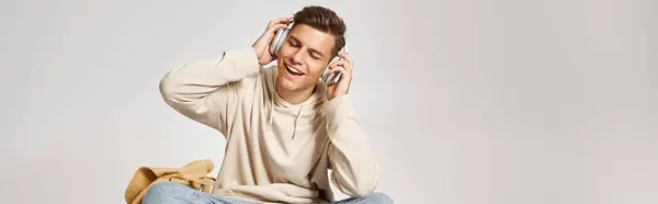Banner of charming man in headphones sitting with backpack and skateboard and listening to music — Stock Photo