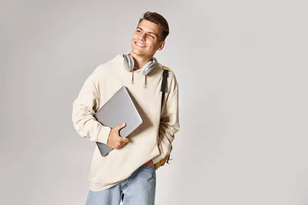 Charming student in his 20s with laptop and headphones walking and looking to side — Stock Photo
