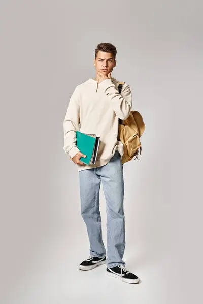 Carismático joven estudiante con mochila sosteniendo notas y tocando la mandíbula con las manos - foto de stock