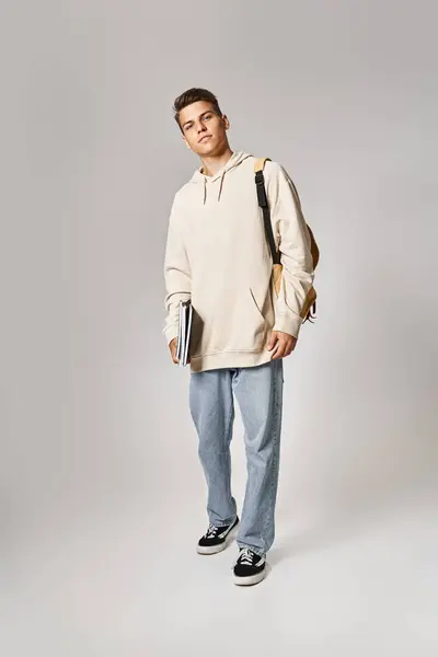 Fröhlicher Student in seinen Zwanzigern mit Rucksack vor grauem Hintergrund — Stockfoto