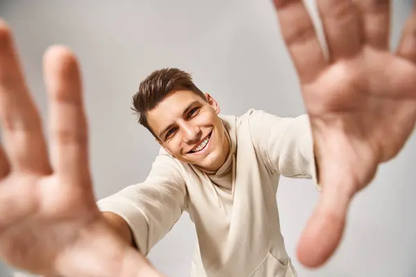 Hombre alegre con el pelo castaño y los ojos grises extendiendo sus manos a la cámara sobre fondo claro - foto de stock