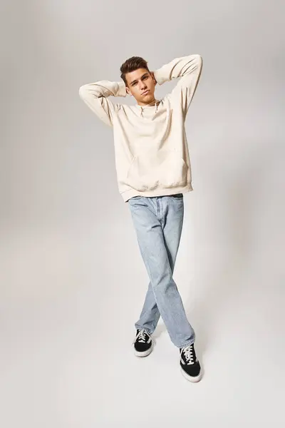 Charming young guy in casual outfit putting hands behind head and standing with cross-legs — Stock Photo