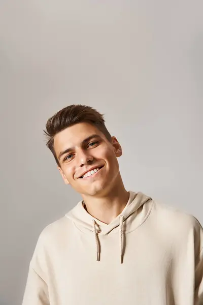 Portrait of smiling young man with brown hair and grey eyes leaning head against light background — Stock Photo