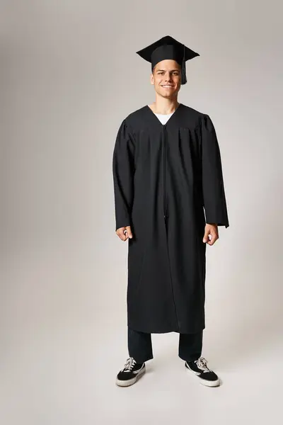 Happy attractive student in graduate gown and cap standing against light background — Stock Photo