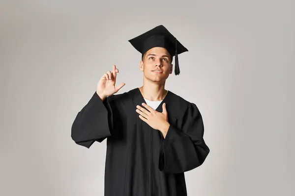Charming young student in graduate gown and cap making wish against grey background — Stock Photo