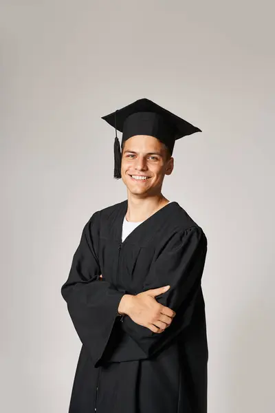 Charming student in graduate gown and cap with folded arms smiling and looking to camera — Stock Photo