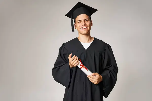 Porträt einer jungen Studentin in Diplomkostüm und Schirmmütze mit den Händen auf grauem Hintergrund — Stockfoto