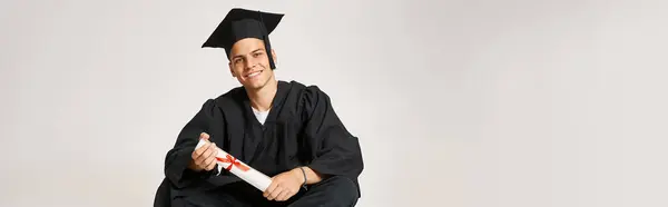 Banner eines glücklichen Mannes in Diplomkleid und Schirmmütze, der mit den Händen am Diplom sitzt — Stockfoto