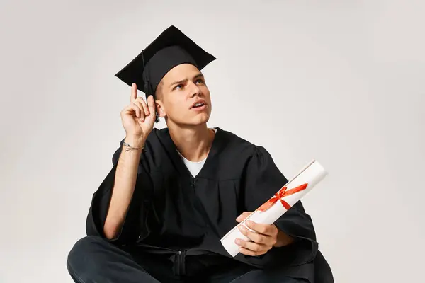 Attractive young student in graduate outfit came up with idea against grey background — Stock Photo