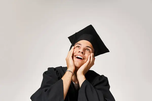 Porträt eines glücklichen, gutaussehenden Mannes mit Diplommütze, der vor grauem Hintergrund bewundernd nach oben blickt — Stockfoto
