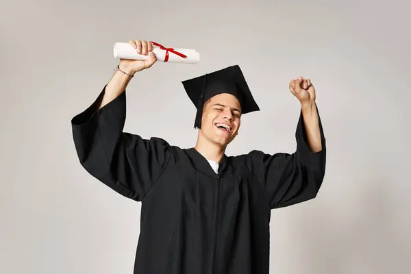 Jovem estudante feliz em roupa de pós-graduação feliz por ter completado seus estudos sobre fundo cinza — Fotografia de Stock
