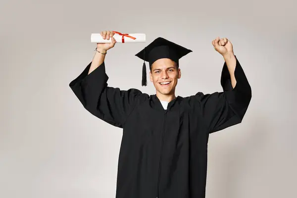 Attraktive Studentin im Diplom-Outfit froh, ihr Studium auf grauem Hintergrund abgeschlossen zu haben — Stockfoto