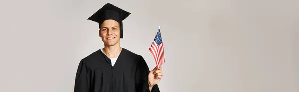 Banner of student in graduate outfit posing with American flag with hand on grey background — Stock Photo