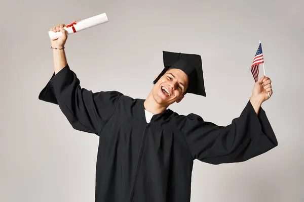 Étudiant américain en tenue d'études supérieures heureux d'avoir terminé ses études sur fond gris — Photo de stock