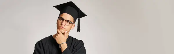 Banner of thoughtful man in graduate outfit and vision glasses touching hand to jawline — Stock Photo