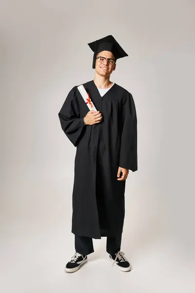 Cheerful student in graduate outfit and vision glasses standing with diploma in hand — Stock Photo