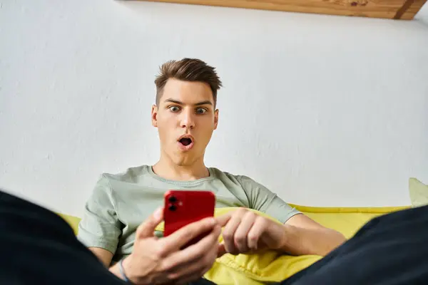 Surprised student in his 20s at home sitting on yellow couch and scrolling in social media — Stock Photo