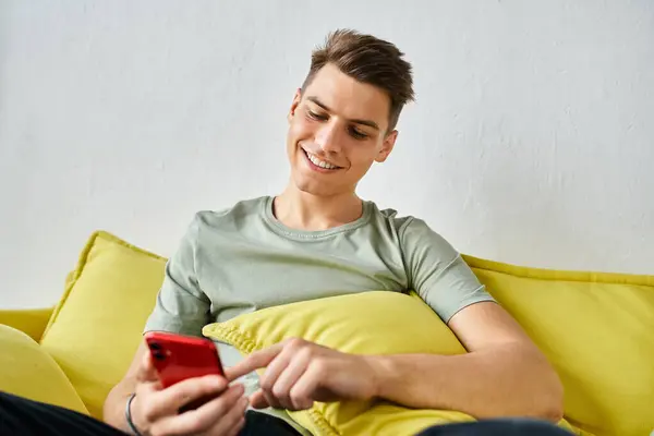 Fröhlicher junger Mann mit braunen Haaren zu Hause auf gelbem Sofa sitzend und in den sozialen Medien scrollend — Stockfoto