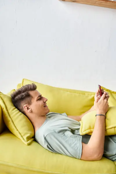 Profile of cheerful student lying on yellow couch in living room and scrolling to social media — Stock Photo