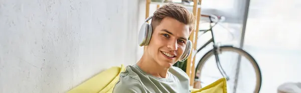 Banner of young man with brown hair in headphones in yellow couch at home looking to camera — Stock Photo