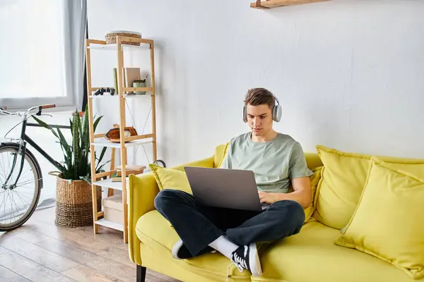 Focused student with brown hair in headphones in yellow couch at home learning on laptop — Stock Photo