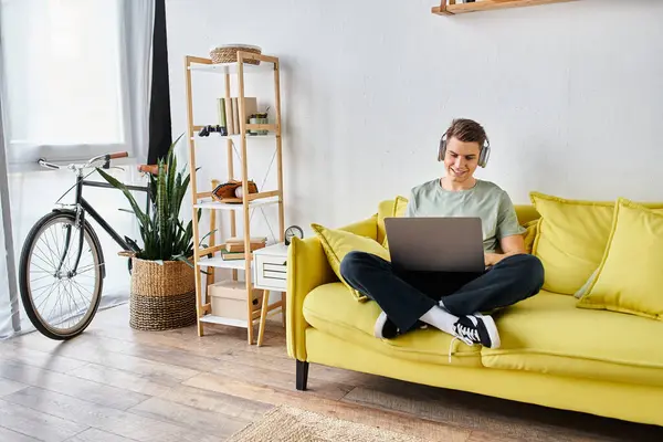 Smiling attractive student in headphones in yellow couch at home studying on laptop — Stock Photo