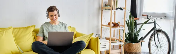 Banner of attractive young man in headphones in yellow couch at home studying on laptop — Stock Photo