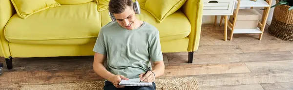 Banner of student with headphones and laptop on floor near yellow couch writing in note — Stock Photo