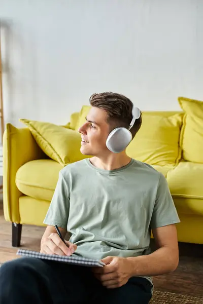 Attraktiver Mann mit Kopfhörern auf dem Boden in der Nähe der gelben Couch — Stockfoto