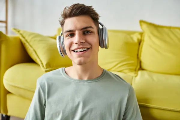 Portrait of smiling charming young man in his 20s with headphones sitting near yellow couch — Stock Photo