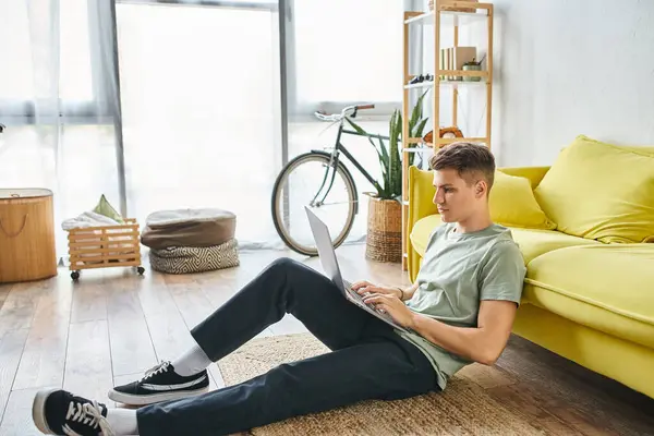Студентка 20-х років з коричневим волоссям на підлозі біля жовтого дивана вдома навчається в стороні ноутбука — стокове фото