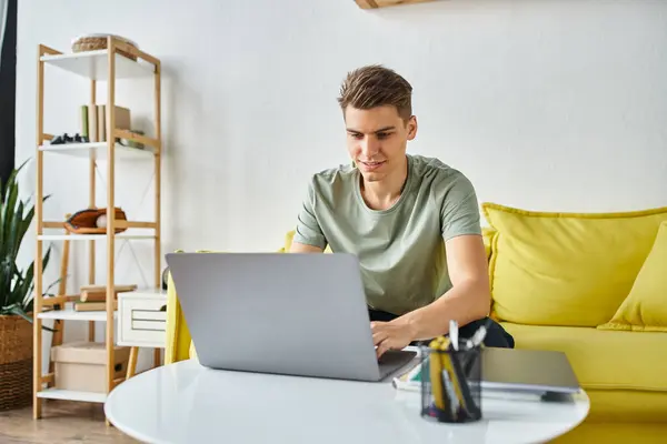 Веселий студент сидить на жовтому дивані вдома мережа в ноутбуці на кавовому столі — стокове фото