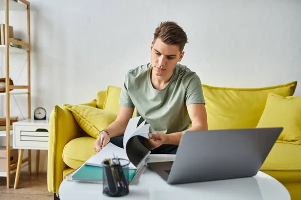 Зосереджений студент в жовтому дивані вдома виконує курсову роботу з ноутбуками і ноутбуком на кавовому столі — стокове фото