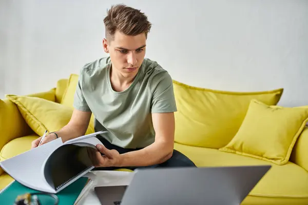 Молодий чоловік в концентрації жовтого дивана виконує курсову роботу з ноутбуками і ноутбуком на кавовому столі — стокове фото