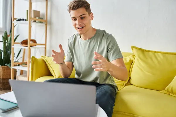 Веселый студент в желтом диване с ноутбуком на кофейном столике рад говорить на онлайн-конференции — стоковое фото