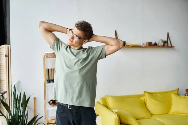 Charming young man with brown hair and vision glasses in living room stretching arms behind head — Stock Photo