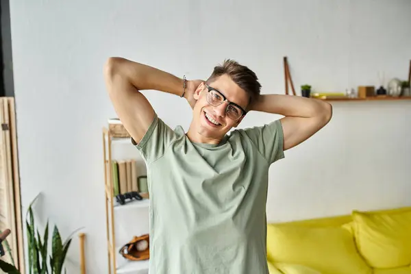 Attractive guy with brown hair and vision glasses in living room putting arms behind head to camera — Stock Photo