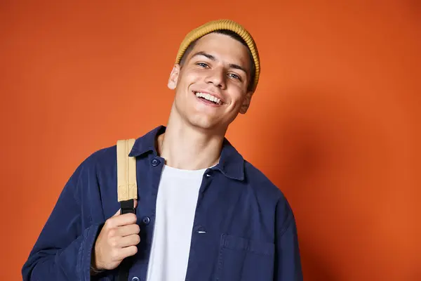 Retrato de chico guapo sonriente en sombrero amarillo con mochila contra fondo de terracota - foto de stock