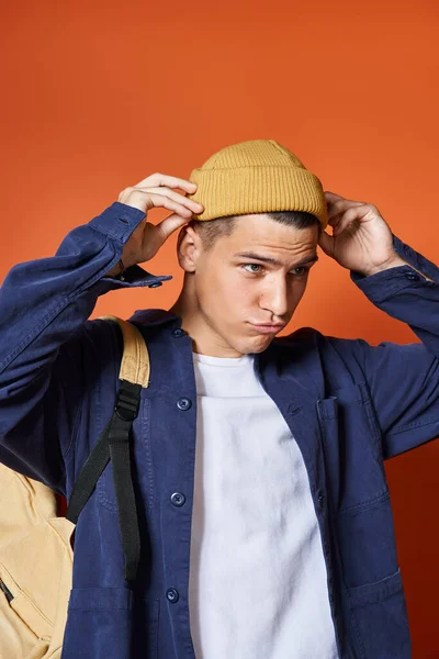 Attractive young man with backpack adjusting his yellow hat on terracotta background — Stock Photo