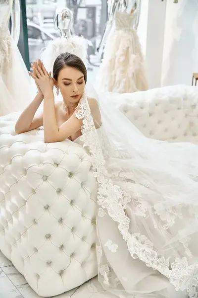 A young brunette bride in a stunning wedding dress resting peacefully on a luxurious bed in a bridal salon. — Stock Photo