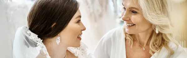 Eine junge Braut im Brautkleid steht mit ihrer Mutter mittleren Alters in einem Brautsalon. — Stockfoto