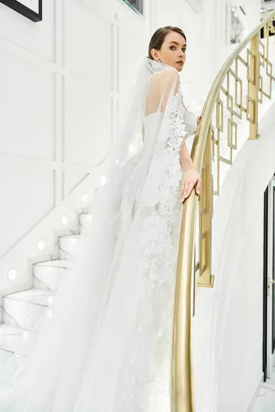 Uma jovem noiva morena em um vestido de noiva fica graciosamente em uma escada — Fotografia de Stock