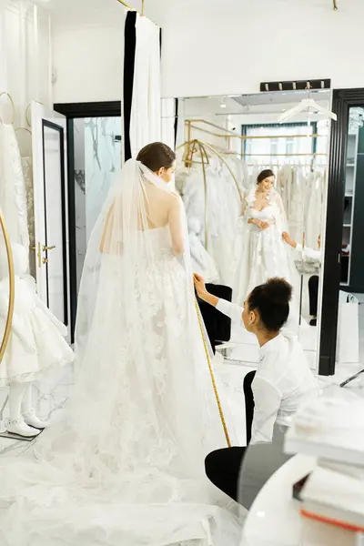 Una joven novia en un vestido de novia blanco conversa con un asistente de compras afroamericano en un lujoso salón nupcial. - foto de stock