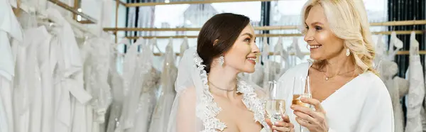 Eine junge Braut im Brautkleid steht neben ihrer Mutter mittleren Alters in einem Brautsalon und teilt einen besonderen Moment. — Stockfoto