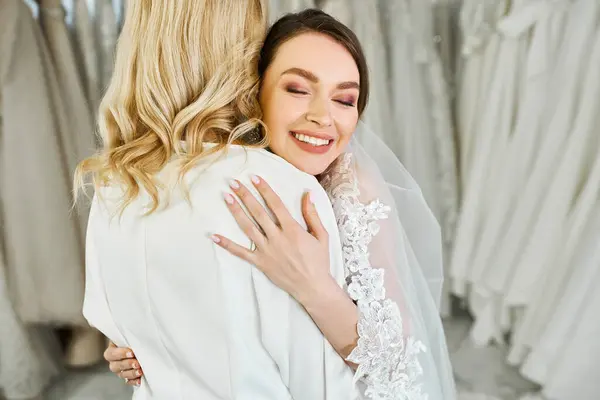 A young bride in a wedding dress lovingly embraces her middle-aged mother in a bridal salon. — Stock Photo
